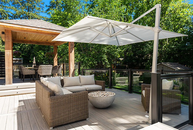 Gorgeous outdoor living space with a custom deck with outdoor furniture, firepit, and pavilion surrounded by a black aluminum glass railing.